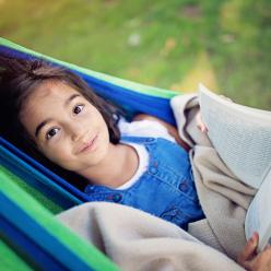 A smiling girl reading in a hammock