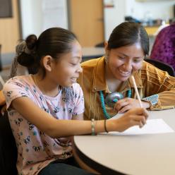 An adult works at a table with a student