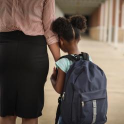 Anxious girl wearing backpack and clutching an adult's arm