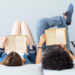 Two teens lying down and reading books.