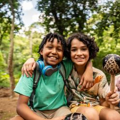 Two kids in the woods smiling at the camera.
