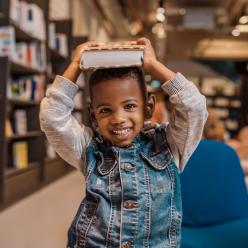 A smiling boy holding a book on his head.