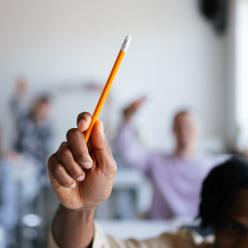 Student raising hand with pencil in class.