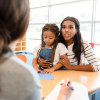A parent holding her daughter while talking to a teacher