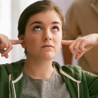 A teen rolling her eyes and with her fingers in her ears