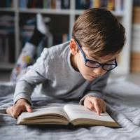 Young child lying down on the floor and reading a book.