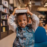 A smiling boy holding a book on his head.
