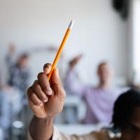 Student raising hand with pencil in class.