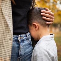 Boy with face buried in his mom's jacket.