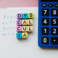 A calculator, math equations, and small blocks that spell out dyscalculia.